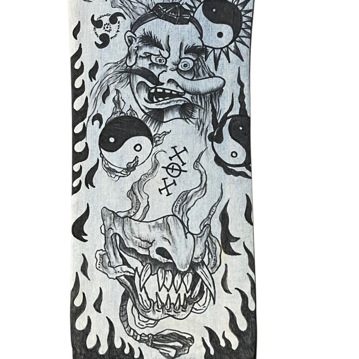 Black and white tattoo design on denim jeans with a creature, yin yang symbols, and flames on a white background.