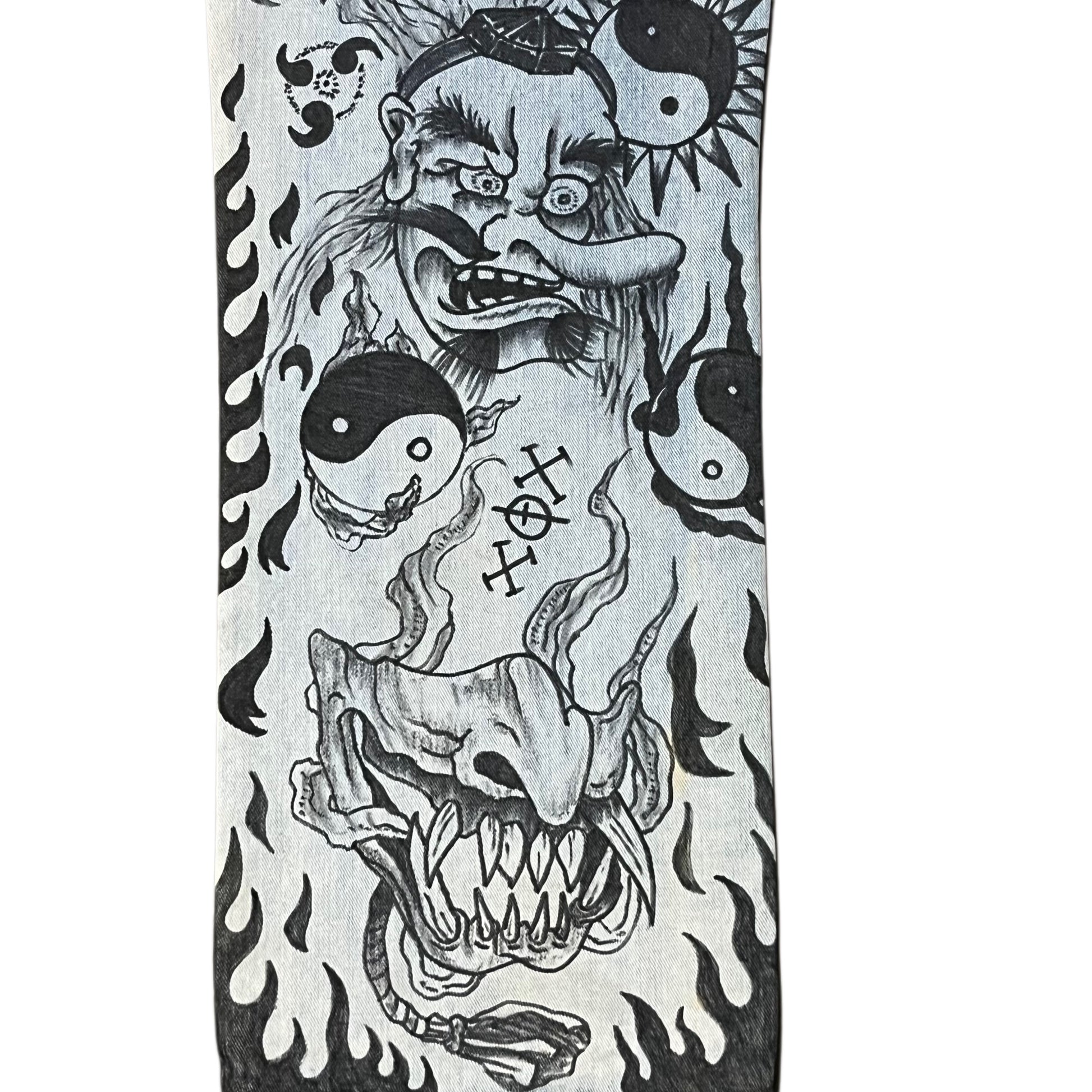 Black and white tattoo design on denim jeans with a creature, yin yang symbols, and flames on a white background.